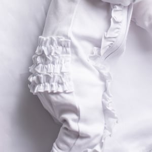 May include: White baby onesie with ruffled trim around the neckline and sleeves. The onesie is made of a soft, comfortable fabric.