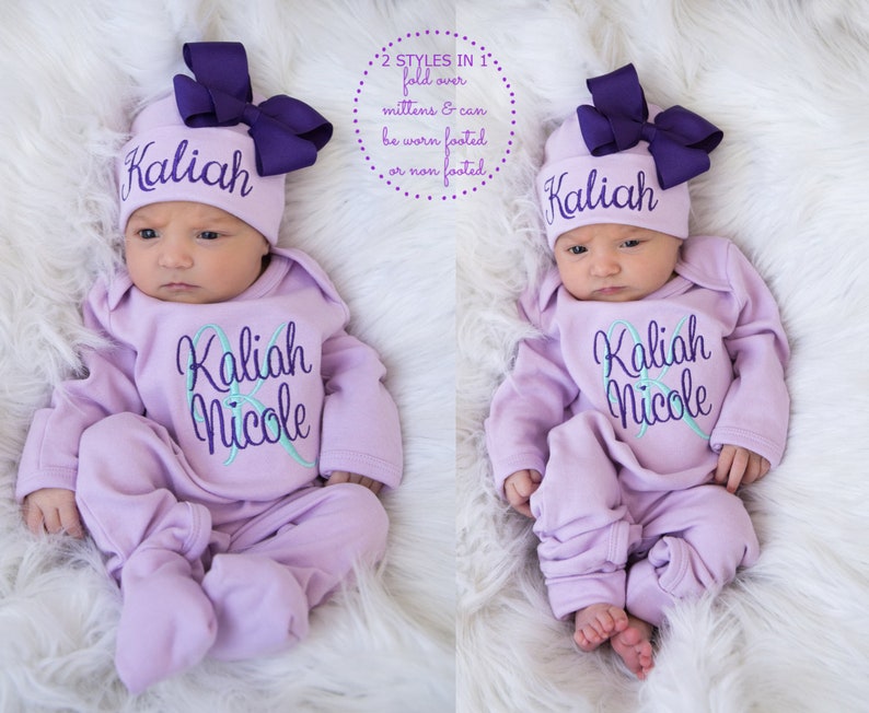 May include: A lavender baby onesie with the names "Kaliah Nicole" embroidered on the front. The onesie has fold-over mittens and can be worn footed or non-footed. The baby is wearing a matching lavender hat with a purple bow and the name "Kaliah" embroidered on the front.