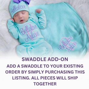 May include: A light blue baby swaddle with the name "Bellalove Arlene" embroidered in purple and pink. The swaddle is folded and placed on a white surface.