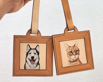 May include: Two leather luggage tags with portraits of a dog and a cat. The tags have a square frame design with a light tan background. The dog is a husky, and the cat is orange with green eyes.