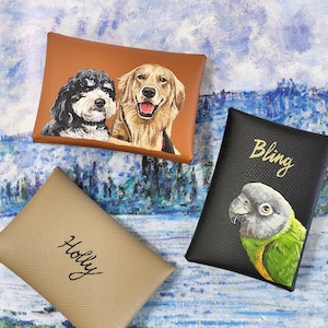 May include: Three leather cardholders with custom pet portraits. One brown cardholder features a black and white dog and a golden retriever. A black cardholder has a parrot illustration and the word "Bling". A tan cardholder has the name "Holly".