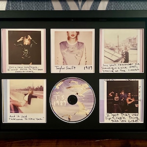 May include: A black framed display with six Polaroid-style photos and a CD. The photos feature images of Taylor Swift, with handwritten captions. The CD is labelled "T.S. 1989". The background is a blue and white pattern.