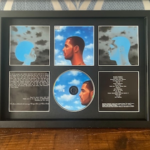 May include: Framed CD and album art featuring a portrait of a man against a blue sky background. The frame includes the CD, album art, and text. The CD has a blue sky design with the man's portrait. The frame is black.