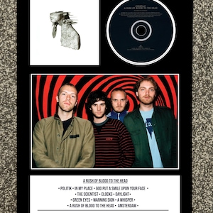 Puede incluir: Presentación enmarcada del álbum "A Rush of Blood to the Head" de Coldplay. La imagen incluye la portada del álbum, un CD y una foto de la banda. La portada presenta una escultura. La foto de la banda muestra a cuatro hombres frente a un fondo en espiral rojo y negro. Se incluye la lista de canciones y los detalles de lanzamiento.