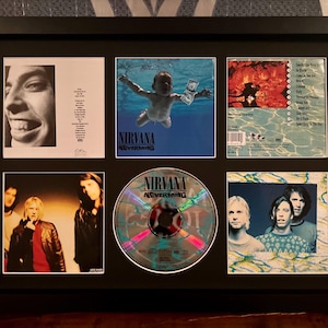 May include: Framed Nirvana "Nevermind" album art and CD. The frame contains the album cover, back cover, and CD, along with other images of the band. The album cover features a baby swimming underwater reaching for a dollar bill.