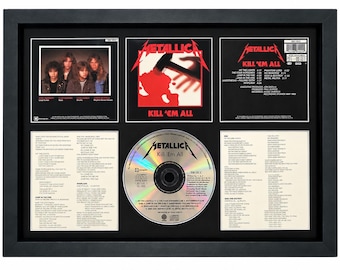 May include: A framed Metallica Kill 'Em All CD display featuring the album cover art, a band photograph, the tracklist, lyrics, and a central disc. The black frame contains white-bordered inserts with the band logo and song titles in black text.