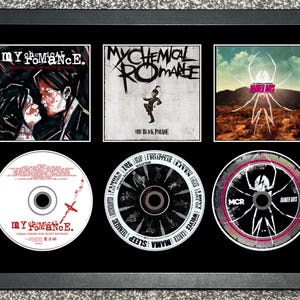 May include: Framed artwork featuring three album covers and three CDs by My Chemical Romance. The album covers include "Three Cheers for Sweet Revenge" and "The Black Parade." The CDs also feature album art.