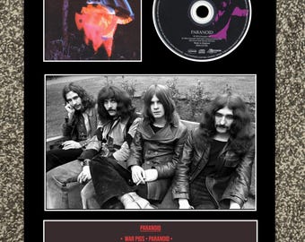 May include: Framed Black Sabbath "Paranoid" album art and CD. The album cover features a red and orange image. A black and white photo of the band is below. The CD is black with purple text. The album's tracklist and release information are also included.