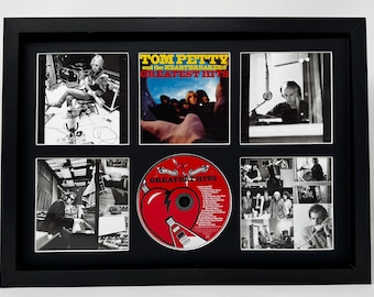 May include: Framed Tom Petty and the Heartbreakers "Greatest Hits" CD and photo collage. The CD is red with a white and black design. The collage includes black and white photos of the band and album art.