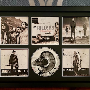 Puede incluir: Obra de arte enmarcada en negro con imágenes en blanco y negro de la banda The Killers. La obra de arte incluye un CD y varias fotografías con el texto "Killers" y "Sam's Town". El marco es negro.