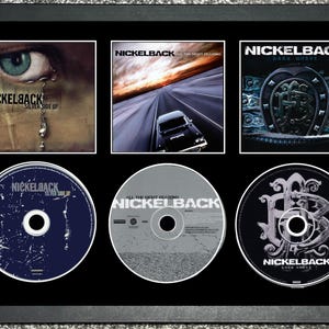 Op de afbeelding: Een ingelijste presentatie met drie Nickelback albumhoezen en drie cd's. De hoezen tonen "Silver Side Up", "All the Right Reasons" en "Dark Horse". De cd's zijn eronder te zien. De lijst is zwart.