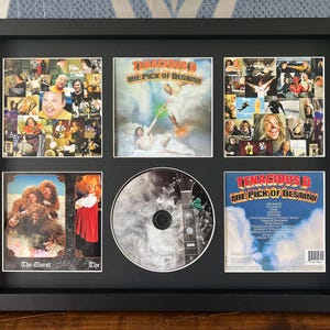 May include: A framed collage featuring a CD and album art from Tenacious D's "The Pick of Destiny" album. The collage includes the CD, album cover, and various images from the band's history, all set within a black frame.