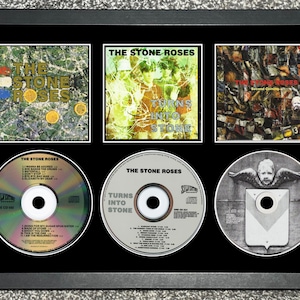 May include: Framed display of The Stone Roses albums and CDs. Three album covers are displayed above three CDs. The album covers and CDs feature the band's name. The frame is black. The CDs are silver.