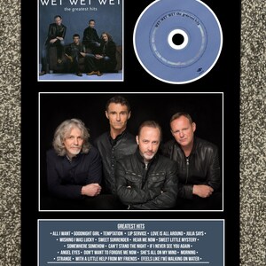 Puede incluir: Un marco con la portada del álbum "Greatest Hits" de Wet Wet Wet y un CD. La portada del álbum presenta una foto grupal de la banda. El CD es azul claro con el nombre de la banda y el título del álbum. El marco incluye una lista de canciones.