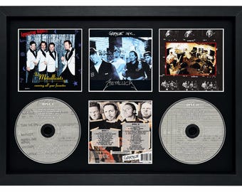 May include: A framed Metallica Garage Inc. double CD set featuring two silver discs, three album art prints, and a central tracklist insert. The display includes the 'Appearing Nightly' cover, the 'Garage Inc.' band photo, and a studio recording scene.