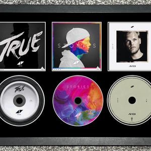 Puede incluir: Un marco negro que exhibe tres portadas de álbumes de Avicii y tres CD correspondientes. La fila superior muestra el arte de True, Stories y Tim. La fila inferior muestra los CD a juego, incluyendo el disco True, el disco colorido Stories y el disco Tim.