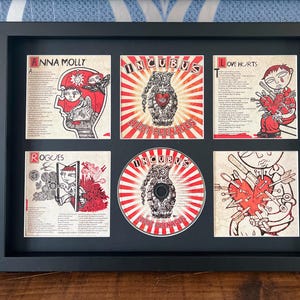 Puede incluir: Obra de arte enmarcada con seis paneles que muestran ilustraciones y texto. El panel central y el arte del CD muestran un diseño rojo y blanco con la palabra "INCUBUS". Otros paneles incluyen letras de canciones y obras de arte en rojo y negro. El marco es negro.