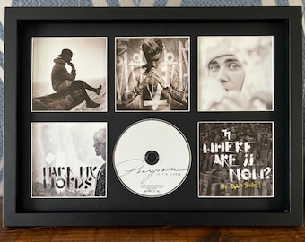 May include: Black framed display featuring six images and a CD. The images are black and white photos of a musician. The CD is white with the word "Purpose" and the artist's name. The frame is rectangular.