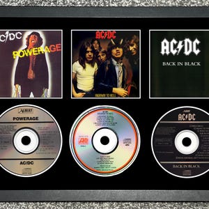 Puede incluir: Exhibición enmarcada con tres portadas de álbumes y tres CD de AC/DC. Los álbumes son "Powerage", "Highway to Hell" y "Back in Black". Los CD también muestran los títulos de los álbumes. El marco es negro.