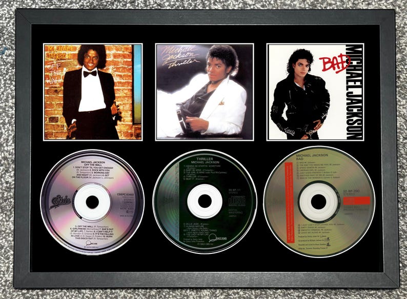 Może przedstawiać: Oprawiona ekspozycja z trzema okładkami album&oacute;w i trzema płytami CD Michaela Jacksona. Okładki album&oacute;w to "Off the Wall", "Thriller" i "Bad". Płyty CD r&oacute;wnież noszą te tytuły. Rama jest czarna.