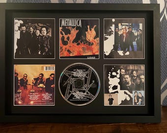 May include: A framed display featuring a Metallica CD and album art prints. The CD is centered, surrounded by six framed images. The album art includes the word "Metallica" and the album title "Load". The images are in black and white and color.