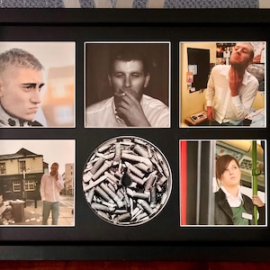 May include: A framed collage featuring six images. Five are photographs of people in various settings, some in black and white. The central image is a CD covered in cigarette butts. The frame is black.