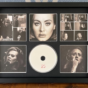 Puede incluir: Un collage enmarcado en negro y blanco con imágenes de una cantante, incluyendo un retrato central y fotos más pequeñas de ella actuando. Un CD con el número "25" está en el centro. El marco es negro.