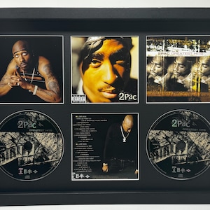 Può includere: Esposizione incorniciata del CD e dell'artwork dell'album "Greatest Hits" di 2Pac. La cornice nera contiene una collezione di immagini, tra cui copertine di CD e ritratti dell'artista. L'esposizione presenta un mix di artwork dell'album e dischi CD.