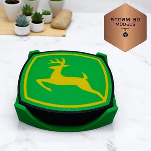 May include: Green and yellow coaster set featuring the John Deere logo, a yellow deer on a green background. The coasters are in a green holder. The logo is outlined in yellow. The coasters are made of a foam-like material.