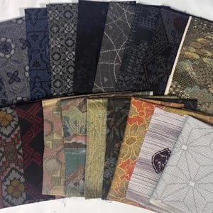 May include: A collection of rectangular fabric swatches arranged in a fan shape. The textiles feature a variety of patterns including geometric shapes, floral motifs, and abstract designs in colors ranging from dark navy and black to gold, red, and white.
