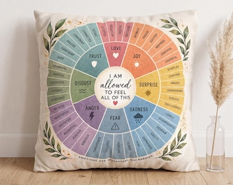 May include: A square throw pillow featuring a colorful emotion wheel graphic with the text "I AM allowed TO FEEL ALL OF THIS" in the center and "EMOTIONS ARE MESSENGERS, NOT ENEMIES" at the bottom, accented by green leaf illustrations on the corners.