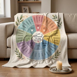 May include: A cream-colored throw blanket featuring a circular emotion wheel graphic with various pastel segments labeled with feelings like love, joy, surprise, sadness, fear, anger, disgust, and trust, with the text I AM ALLOWED TO FEEL ALL OF THIS.