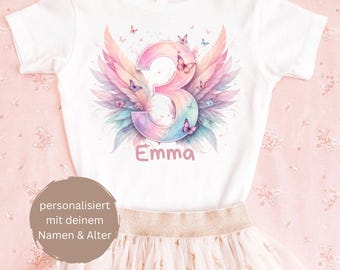 Puede incluir: Una camiseta blanca de manga corta con un número 3 grande en colores pastel degradados, rodeado de alas estilo acuarela y pequeñas mariposas. El nombre Emma está impreso en rosa debajo del número. Incluye una falda rosa con estrellas doradas.