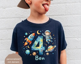 May include: A navy blue t-shirt featuring a colourful space-themed graphic with a large number four, a rocket ship, an astronaut, planets, stars, and the name Ben printed in light blue. The design includes a circular badge with German text.