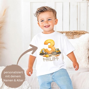 Könnte beinhalten: Ein weißes T-Shirt mit kurzen Ärmeln, das eine Grafik mit einer großen orangefarbenen Zahl 3, gelben Baustellenfahrzeugen und dem Namen PHILIPP in braunen Buchstaben zeigt. Das Motiv enthält einen gelben Bauhelm und orange Pylonen.