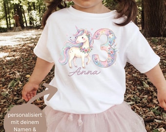 Puede incluir: Camiseta blanca con un diseño de unicornio en colores pastel arcoíris, detalles florales y el número 3. El nombre "Anna" está escrito debajo. La camiseta la lleva un niño.