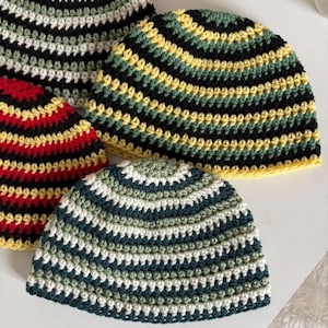 May include: Four handmade crochet beanies in various color combinations. One beanie features black, white, and green stripes. Another has red, yellow, and black stripes. The other two beanies have green, white, and black stripes, and yellow, green, and black stripes.