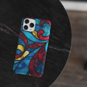 Può includere: Una custodia per smartphone con un design a vetrata. La custodia presenta un vivace motivo di colori blu, rosso e giallo. La custodia è su una superficie scura e strutturata.