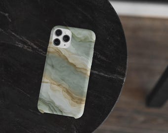 以下が含まれることがあります： 緑、ベージュ、白の色合いの大理石模様のスマートフォンケース。ケースは暗く、質感のある表面に置かれています。携帯電話ケースには、3つのレンズを備えたカメラモジュールがあります。