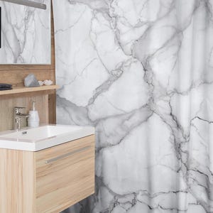 May include: White and gray marble-patterned shower curtain. The curtain hangs from a white rod and features a realistic veining design. The bathroom also includes a wooden vanity, a white sink, and a mirror.