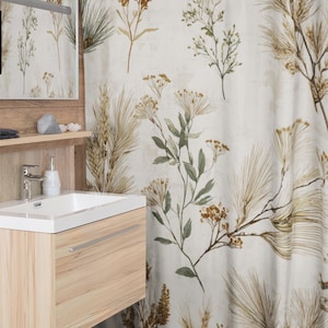 Könnte beinhalten: Beigefarbener Duschvorhang mit botanischem Design mit Illustrationen von Weizen, Blättern und Blumen in Braun-, Grün- und Goldtönen. Der Vorhang hängt vor einem hellen Holzwaschtisch mit einem weißen Waschbecken und einem Spiegel.