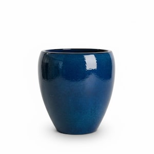Könnte beinhalten: Ein tiefblauer, abgerundeter Keramikübertopf mit glänzender, reflektierender Oberfläche. Das Gefäß hat eine weite Öffnung und eine glatte, geschwungene Silhouette, die sich zur Basis hin leicht verjüngt und eine gleichmäßige Kobaltfarbe aufweist.