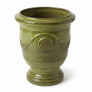 Może przedstawiać: Glazurowana ceramiczna urna w żywym oliwkowozielonym odcieniu z błyszczącym wykończeniem. Naczynie posiada szeroki, rozszerzany brzeg, zwężany korpus i okrągłą podstawę. Wypukły medalion oraz girlandy zdobią zewnętrzną powierzchnię przedmiotu.