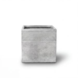 Könnte beinhalten: Ein quadratischer, grauer Betonblumentopf mit einem strukturierten, horizontal gestreiften Design im oberen Bereich. Der Pflanztopf hat eine schlichte, moderne Ästhetik und ist für den Innen- und Außenbereich geeignet. Der Pflanztopf hat eine Würfelform.