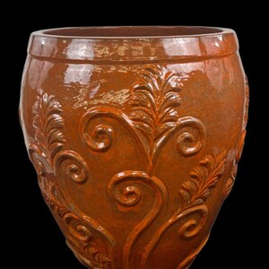 Peut inclure: Un grand pot de fleurs en céramique émaillée de forme ronde, d'une couleur orange brûlé profond. La surface extérieure présente un motif en relief composé de vignes tourbillonnantes et de feuilles rappelant des fougères sur tout le corps.