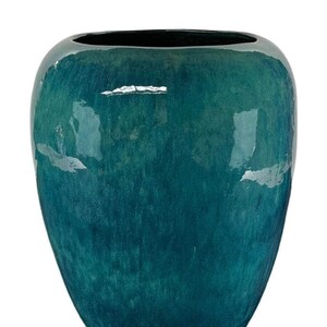 Peut inclure: Un vase en céramique de couleur sarcelle avec une finition brillante. Le vase a un corps large et arrondi qui se rétrécit vers la base et un intérieur sombre. La surface reflète la lumière, soulignant les variations de couleur. Ce vase décoratif convient à la décoration intérieure.