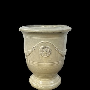Peut inclure: Pot de fleurs en céramique beige clair avec un large bord et une base en piédestal. Le pot présente un emblème décoratif et des lignes horizontales autour du corps. Le design comprend des détails en forme de corde de chaque côté de l'emblème.