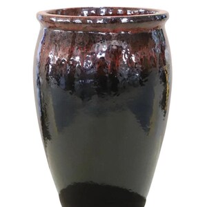 Może przedstawiać: Błyszczący, ciemny ceramiczny wazon. Górna krawędź jest czerwonobrązowa, przechodząca w głęboką czarną podstawę. Powierzchnia odbija światło, podkreślając fakturę szkliwa. Ten dekoracyjny wazon nadaje się do użytku wewnątrz i na zewnątrz. Wysokość: ok. 30 cm.