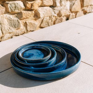 Peut inclure: Ensemble de quatre plats de service ronds en céramique émaillée de différentes tailles. Les plats sont d'un bleu profond et brillant, avec une surface légèrement texturée et un bord plus foncé. L'arrangement suggère qu'ils sont conçus pour le stockage ou l'exposition.