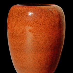 Peut inclure: Un grand vase en céramique orange avec une texture tachetée. Le vase a un corps large et arrondi qui se rétrécit légèrement vers la base. L'ouverture est large et circulaire. Le fond est noir.